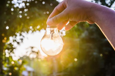 A hand holding up a light bulb with the sun shining through it