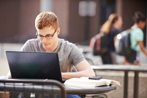 A student at an outdoor table looking at a laptop screen