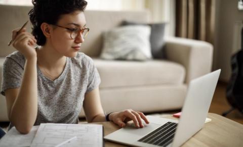 A woman holding a pencil and using a laptop